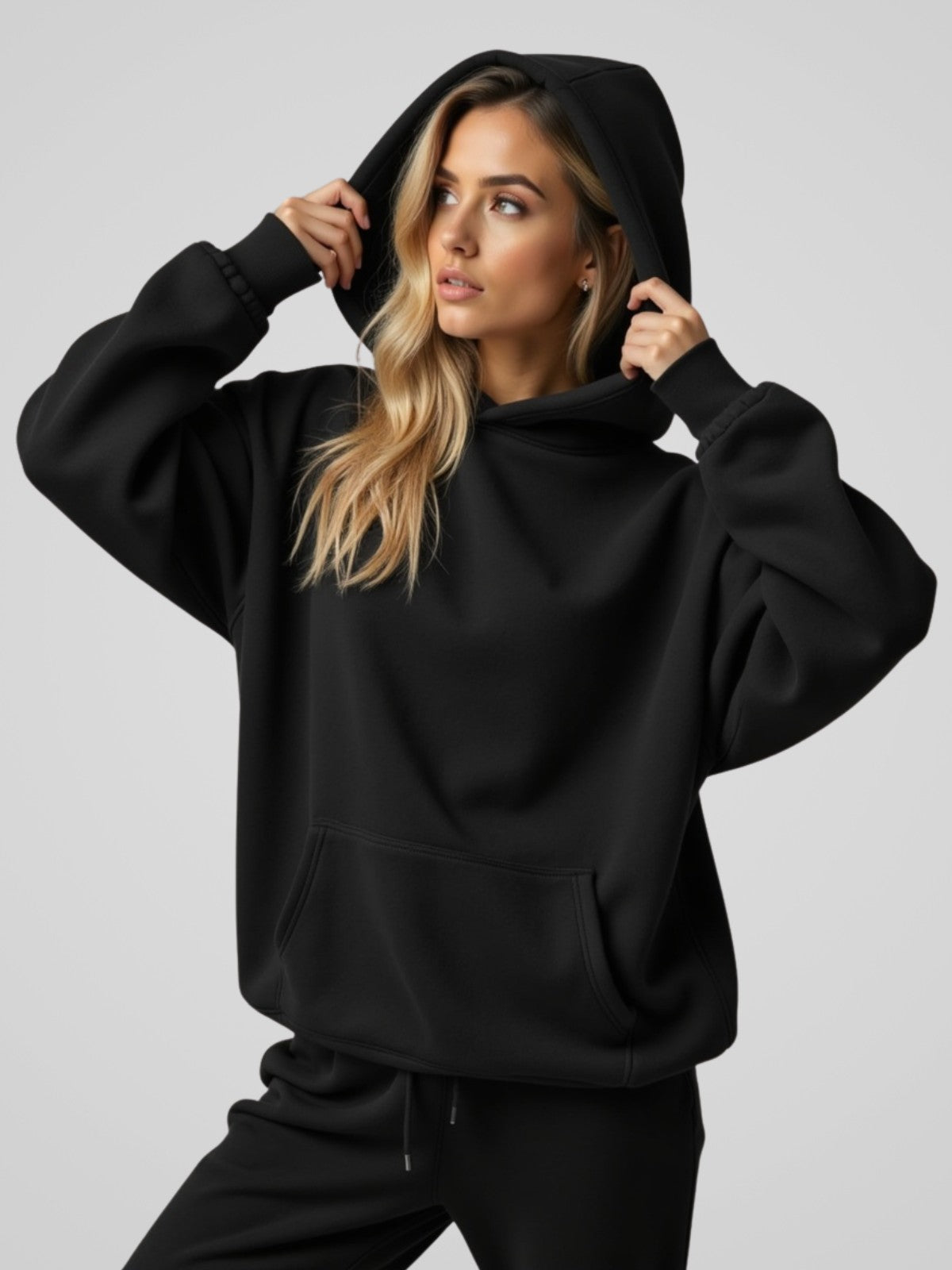 Woman wearing a black oversized hoodie with the hood up, standing and facing forward to show the fit and style.